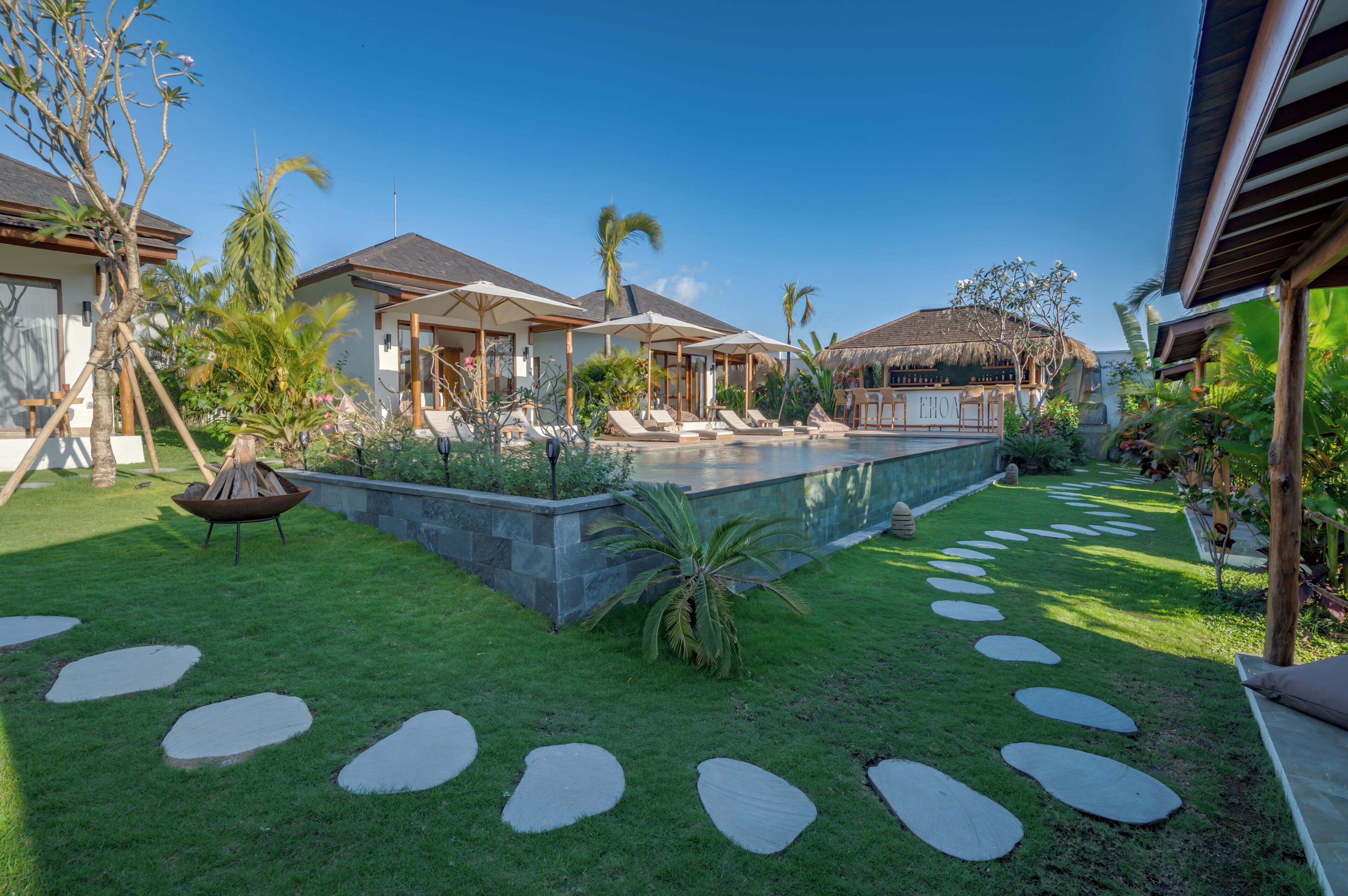 A pool area with lounge chairs, a thatched-roof structure, and a stone pathway.