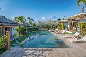 Ein Poolbereich mit Liegestühlen und Sonnenschirmen, umgeben von tropischen Pflanzen und einer Holzterrasse.