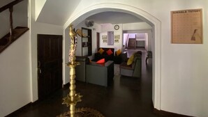 An interior with a staircase, a central seating area with cushions, a wall-mounted clock, and a framed board on the wall. - Kudaarala Heritage (Kengalla)