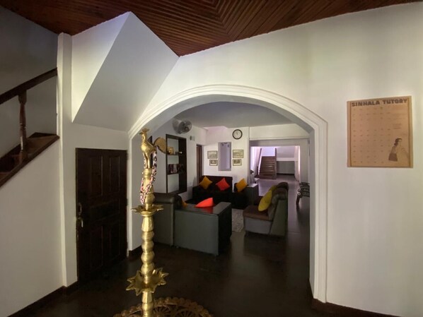 An interior with a staircase, a central seating area with cushions, a wall-mounted clock, and a framed board on the wall.