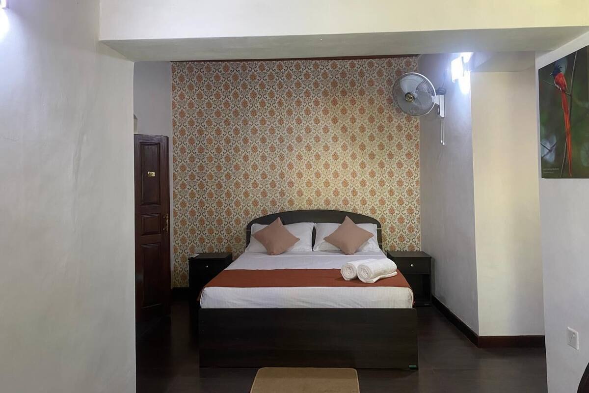 A bedroom with a bed, a nightstand, a wall-mounted fan, and a door.