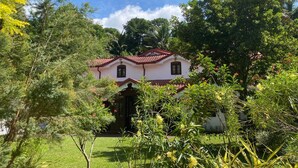 A two-story house with a red-tiled roof, surrounded by lush greenery and trees. - Kudaarala Heritage (Kengalla)