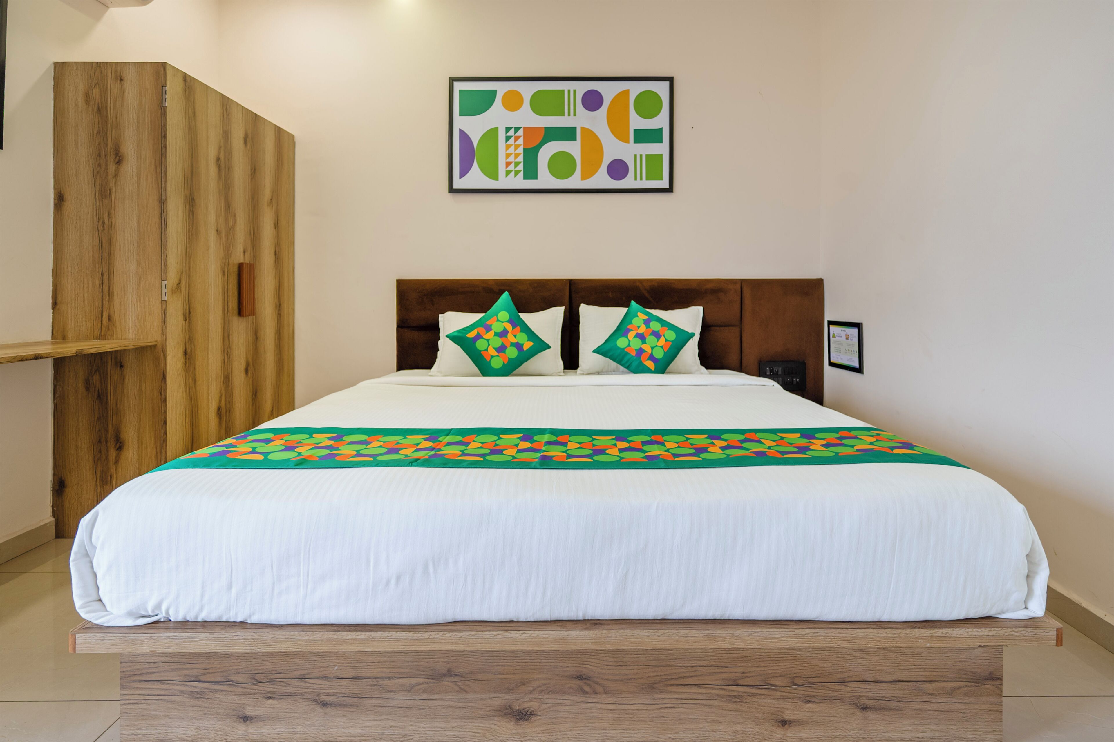 Una cama con sábana blanca, dos almohadas de estampado geométrico, cabecera de madera y un armario de madera.