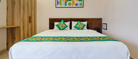 Una cama con sábana blanca, dos almohadas de estampado geométrico, cabecera de madera y un armario de madera.