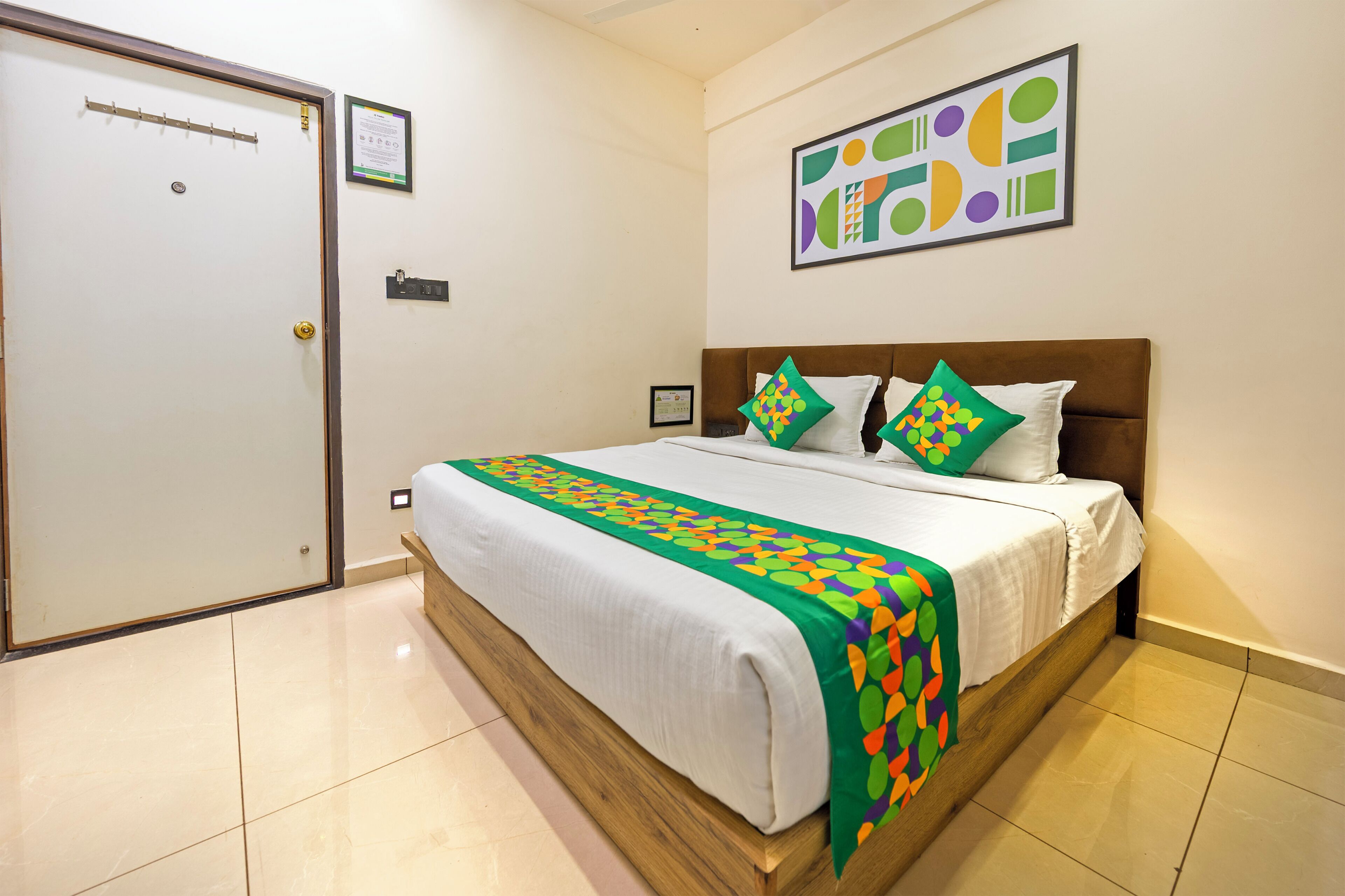 Quarto de hotel com uma cama, uma porta, uma obra de arte abstrata emoldurada e um pequeno certificado na parede.