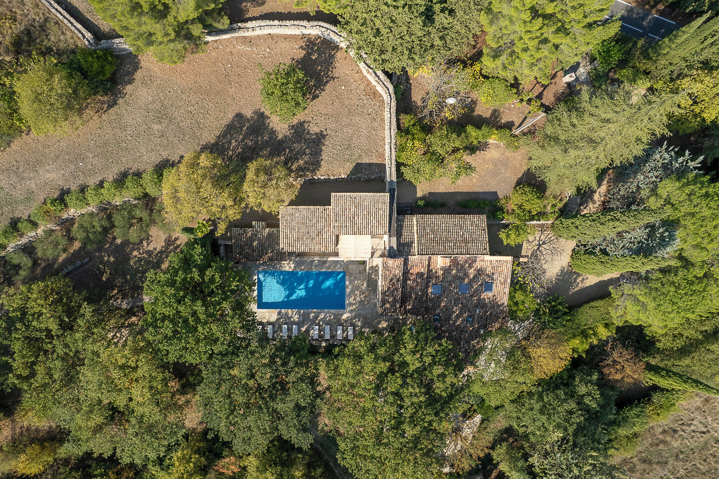 An aerial view of a property with a swimming pool, surrounded by dense greenery and a stone wall.