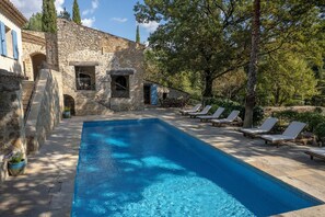 Ein Steinhaus mit Swimmingpool und Liegestühlen.