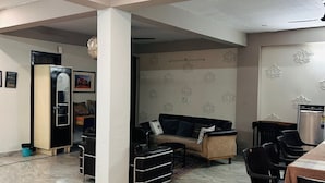 A spacious living area with a sofa, dining table, and chairs. There is a refrigerator and a microwave in the kitchen area. - Abhi Ganga Homestay (Haridwar)
