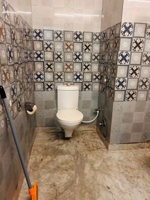 Une salle de bain avec des toilettes, une douche et un balai appuyé contre le mur.