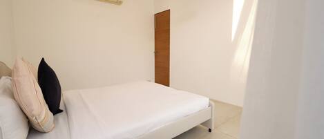 A bedroom with a bed, a wall-mounted air conditioner, a wooden door, and a hanging light fixture.