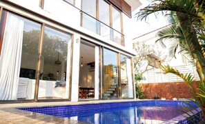 A modern house with a large glass door, a swimming pool, and a garden with palm trees. - Sun Contemporary by Dia Homes (Nerul)