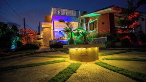 A modern house with a well-lit front yard, a central light feature, and a decorative fence.