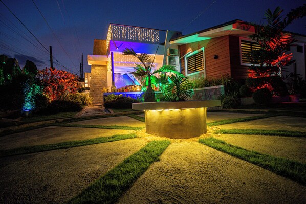 A modern house with a well-lit front yard, a central light feature, and a decorative fence.