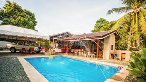 A swimming pool with a covered patio area, a truck, and outdoor furniture.