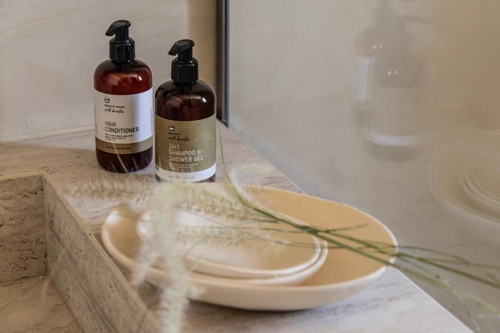 Twee flessen haarkonditionering en shampoo op een marmeren aanrecht, met een bord en een takje gras.