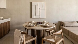 A round dining table with six chairs, a white abstract painting on the wall, and a beige sofa in the background.