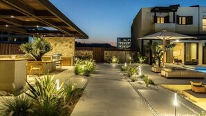 A modern outdoor patio area with a pool, seating, and a stone wall.
