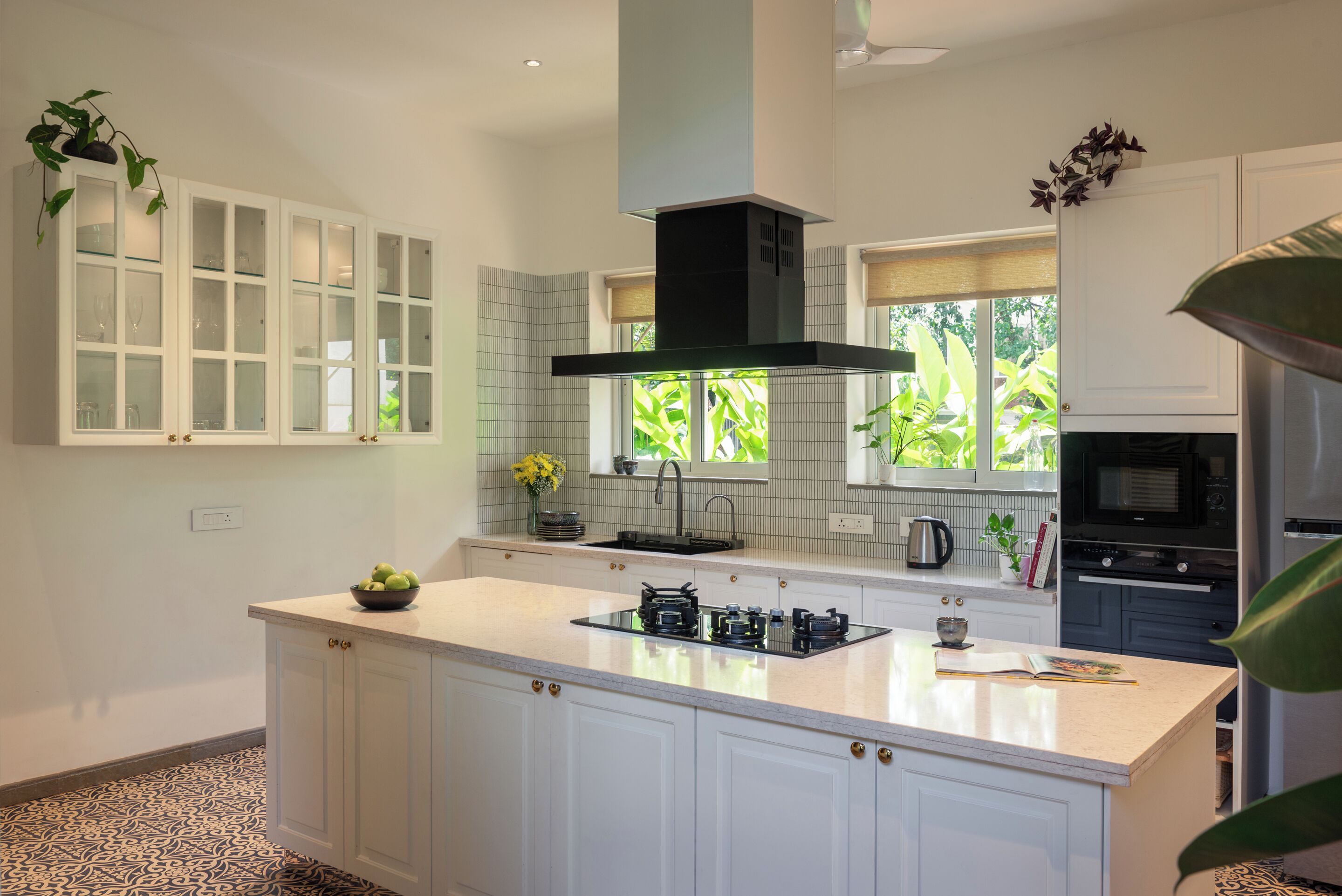 A modern kitchen with a large island, white cabinetry, a black range hood, and a window with a view of greenery.