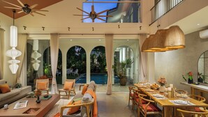 A spacious indoor area with a dining table set for six, a sofa, and a pool visible through the glass doors. - TBK VILLA VAGATOR   01 (Vagator)