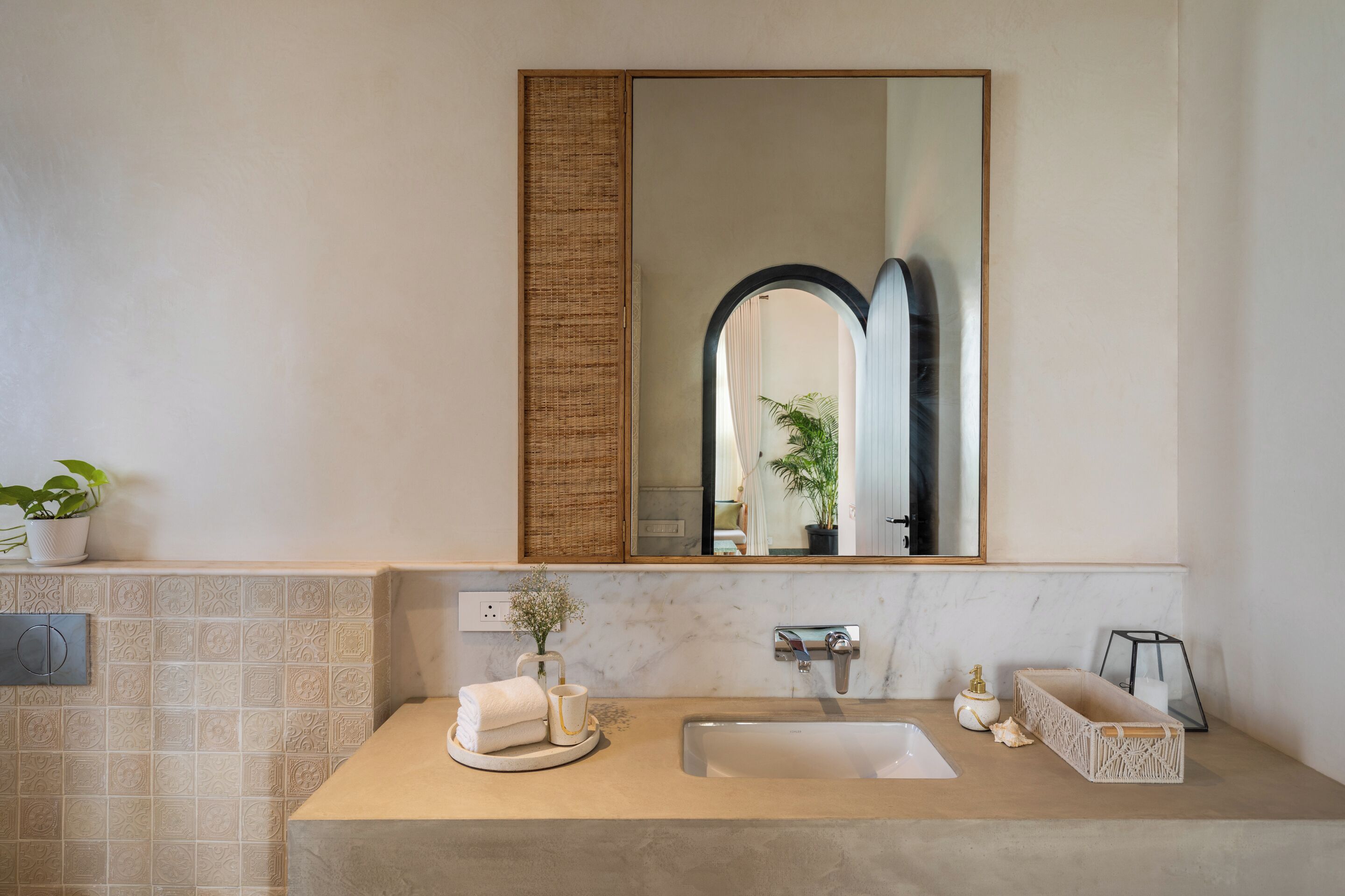 Un baño con lavamanos de mármol, un espejo grande y una planta en maceta.