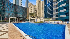 A swimming pool with a tiled deck, surrounded by high-rise buildings. - Bloomfields Signature 1BR Bay Central We (Dubai)