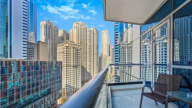A balcony with a view of tall buildings, a chair, and a small table. - Bloomfields Signature 1BR Bay Central We (Dubai)