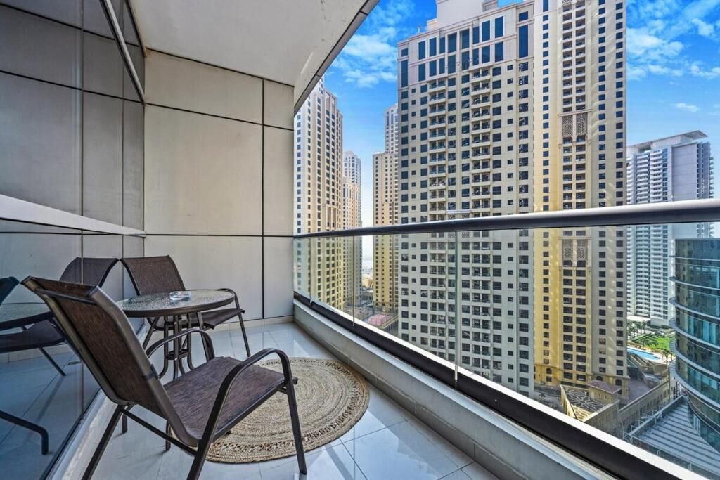 Un balcón con mesa y sillas, vista a edificios altos y cielo despejado.