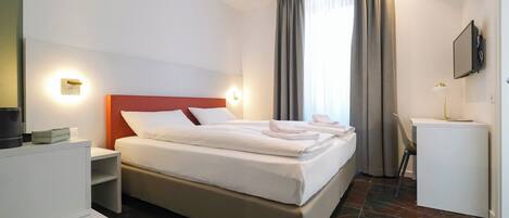 A hotel room with a bed, bedside tables, a desk, a chair, a TV, and a window with curtains.