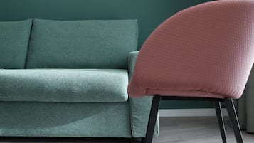 En tealgrøn sofa med en lyserød lænestol i et rum med grøn væg og trægulv.
