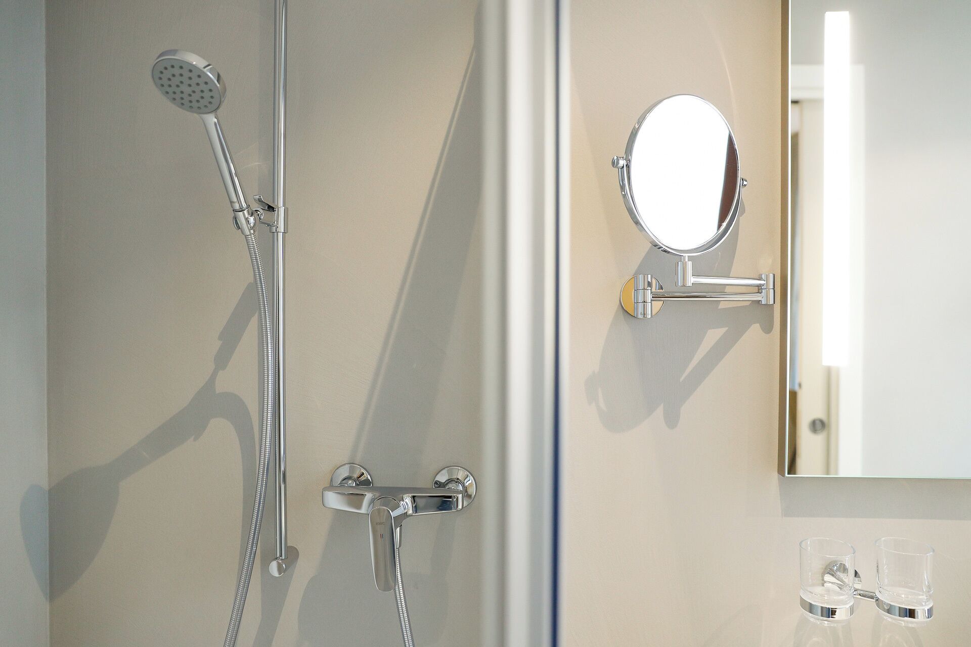 A bathroom with a shower, a mirror, and two clear glasses on the counter.