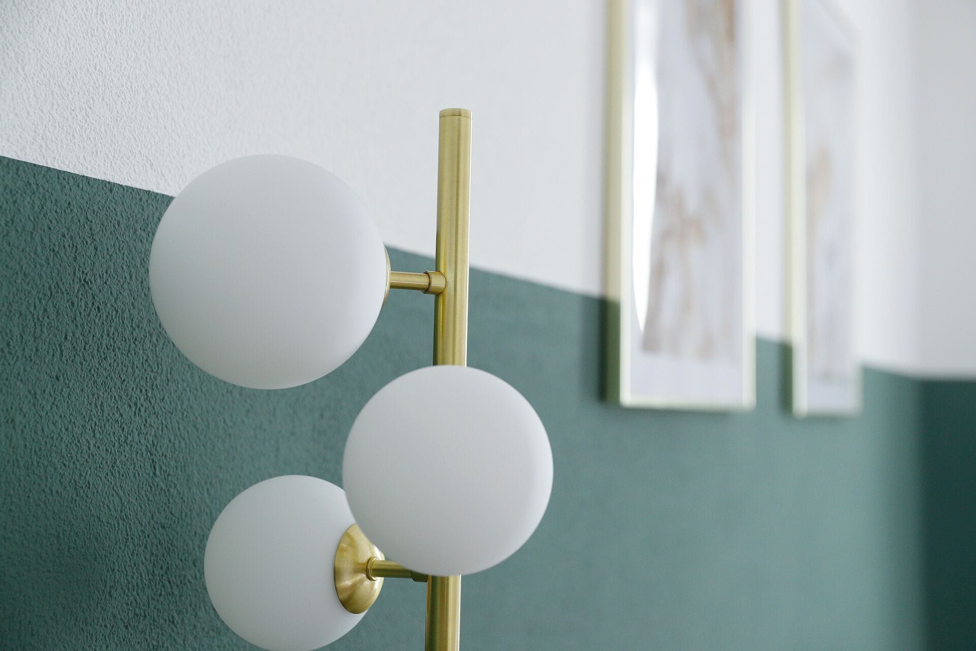 A wall-mounted light fixture with three spherical shades and a gold-colored base.