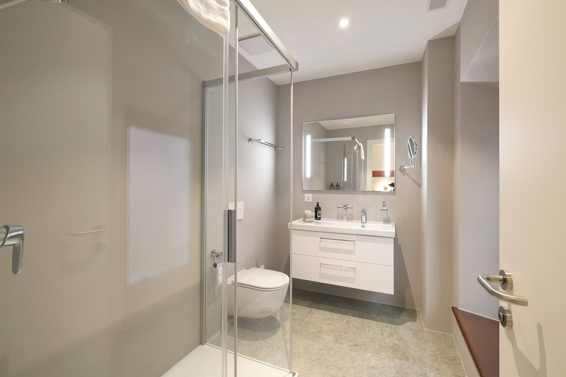 Un baño moderno con cabina de ducha de vidrio, inodoro blanco, tocador con espejo y lavamanos.