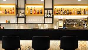 A bar area with shelves of liquor bottles, glasses, and a coffee machine. There are three black chairs in front. - Boutique Hotel Piazza Grande Locarno  (Locarno)