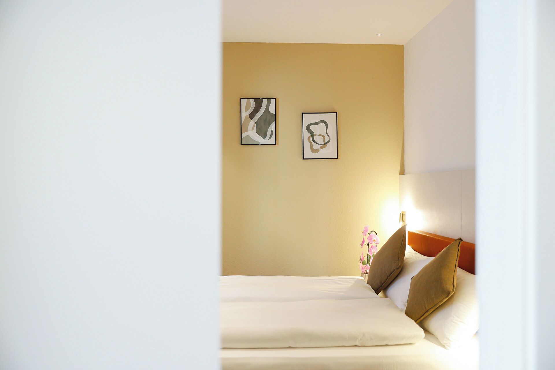 Ein Hotelzimmer mit einem Bett, zwei gerahmten abstrakten Bildern an der Wand und einer Nachttischlampe.