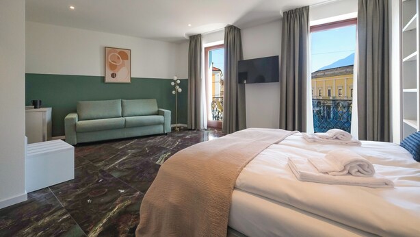 A hotel room with a bed, a sofa, a TV, and a view of the outside. - Boutique Hotel Piazza Grande Locarno  (Locarno)