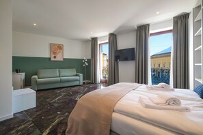 A hotel room with a bed, a sofa, a TV, and a view of the outside.