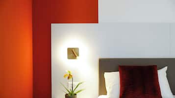 Habitación de hotel con cama, mesita de noche con planta en maceta y lámpara fijada a la pared.