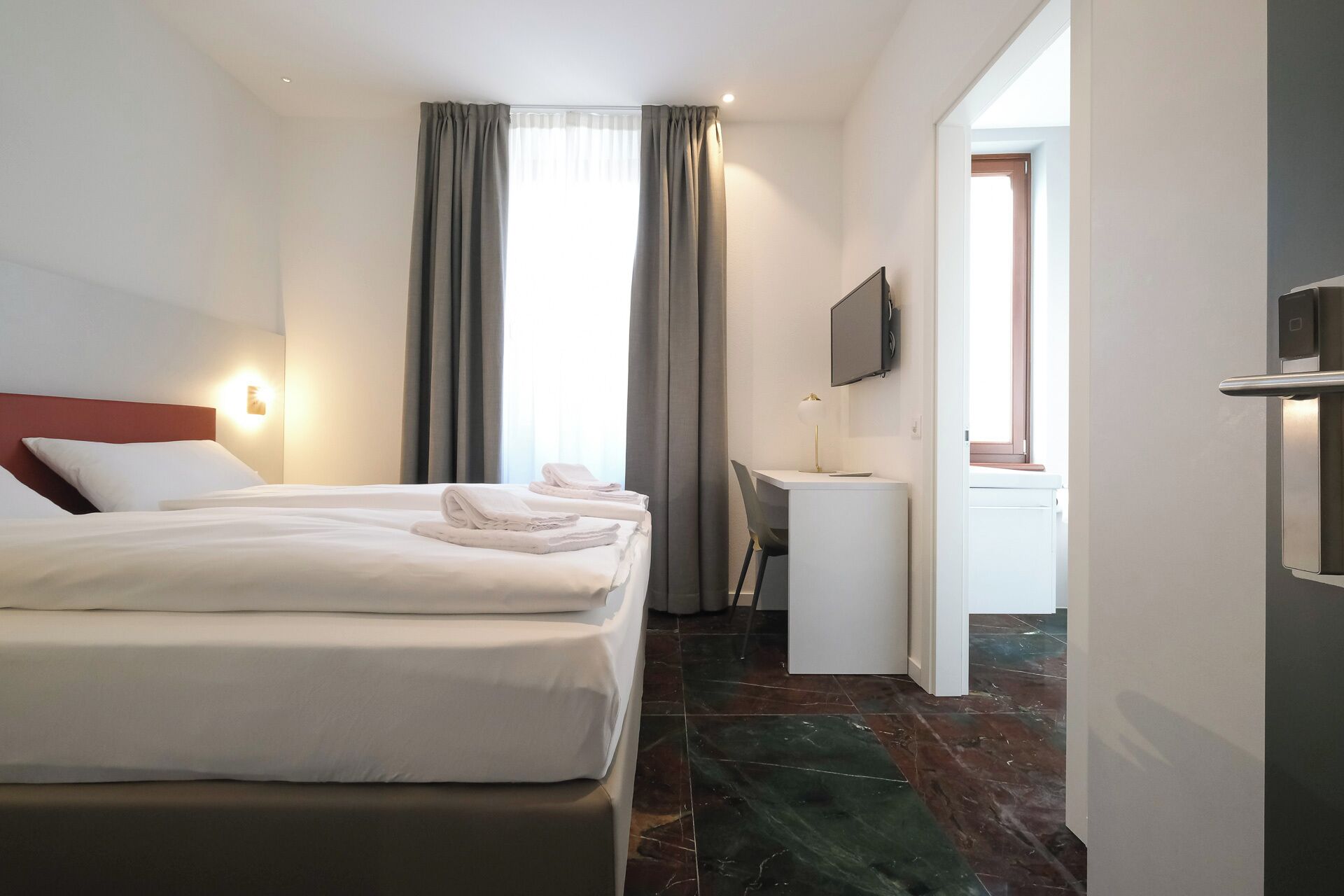 Une chambre d’hôtel avec un lit, un bureau, une chaise, une télévision et une porte de salle de bain.