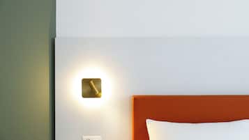 Une chambre d’hôtel avec un mur blanc, une horloge murale de couleur dorée, une tête de lit orange et un oreiller blanc.