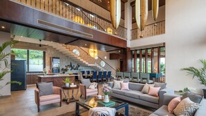 A spacious living area with a staircase, modern furniture, and large windows.