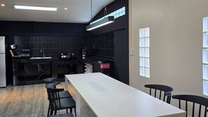 Une cuisine moderne avec un long comptoir blanc, des chaises noires et un banc.