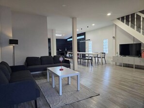 Una sala de estar moderna con un sofá, una mesa de centro y un televisor. Se ve una escalera que sube a un nivel superior.