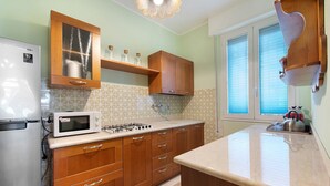 Cozinha com geladeira, micro-ondas, fogão, armários de madeira e janela com persianas.