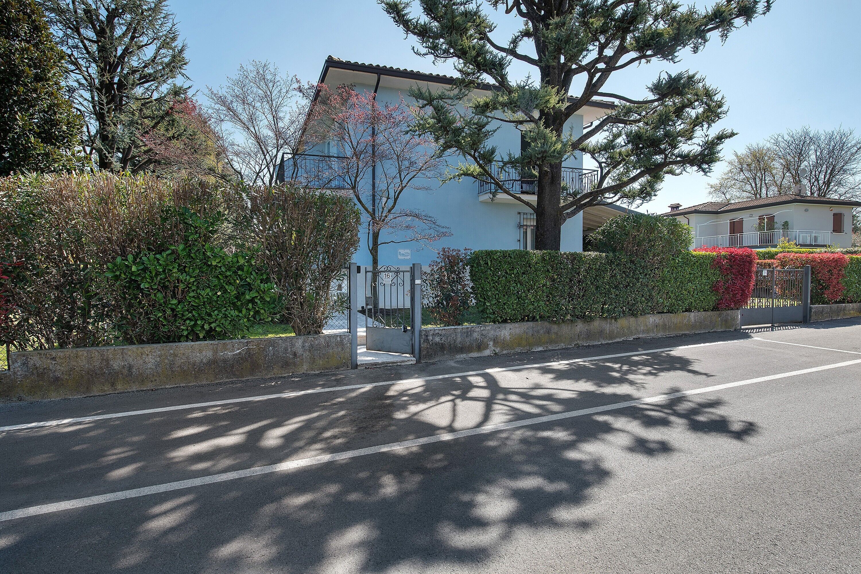 Une rue résidentielle avec un immeuble bleu, une entrée fermée par un portail et un arbre qui projette son ombre sur la chaussée.