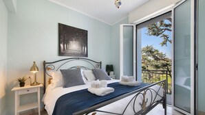 Quarto com cama, mesa de cabeceira, abajur e vista para o exterior.