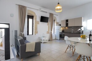 A modern living room with a sofa, a dining table with chairs, a kitchen area with cabinets and a TV, and a large window with curtains. - [NEW] J & I Rooftop Retreat in a small village (89H2+F36 Karoti, Greece)