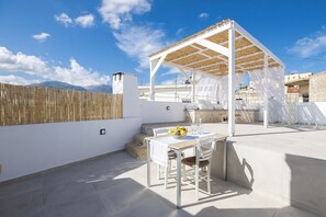 A rooftop terrace with a covered seating area, a table with a bowl of fruit, and a view of mountains in the background. - [NEW] J & I Rooftop Retreat in a small village (89H2+F36 Karoti, Greece)
