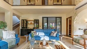 A spacious living area with a blue sofa, a coffee table with decorative items, and a staircase leading to an upper level. - ELIVAAS Casa Bonita 4BHK Villa With Pool (Marra)