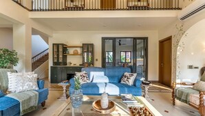 A spacious living room with a blue sofa set, a coffee table with decorative items, and a staircase leading to an upper level. - ELIVAAS Casa Bonita 4BHK Villa With Pool (Marra)