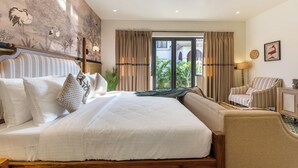 A hotel room with a large bed, a sofa, a chair, a view of greenery outside, and a mural on the wall. - ELIVAAS Casa Bonita 4BHK Villa With Pool (Marra)